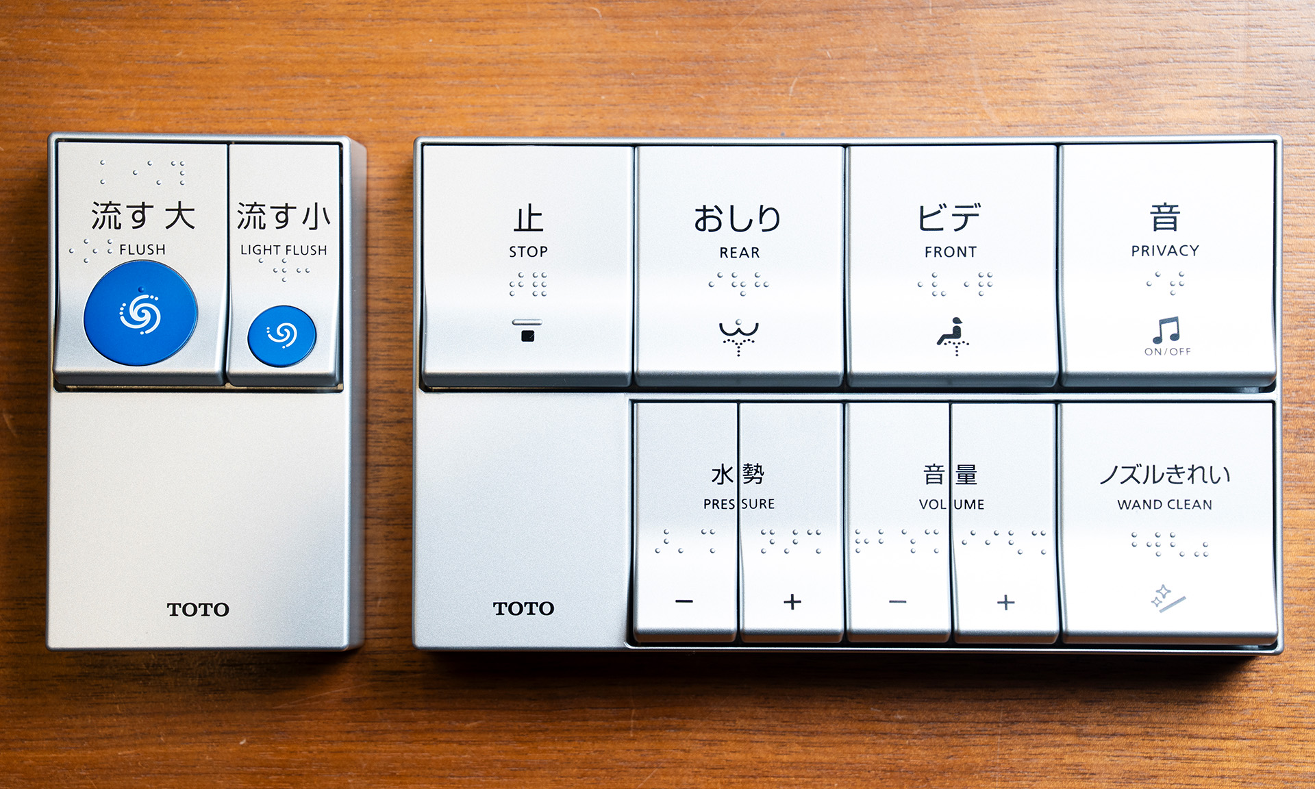 改良前のエコリモコン。便器洗浄リモコンとウォシュレットリモコン。色はシルバーで、文字の色は黒。便器洗浄ボタンは「流す大」「流す小」の2つに分かれていて、それぞれボタン中央に青色の丸い     突起がある。ウォシュレットリモコンのボタンは上下二段に分かれていて、どちらも同じ大きさ
