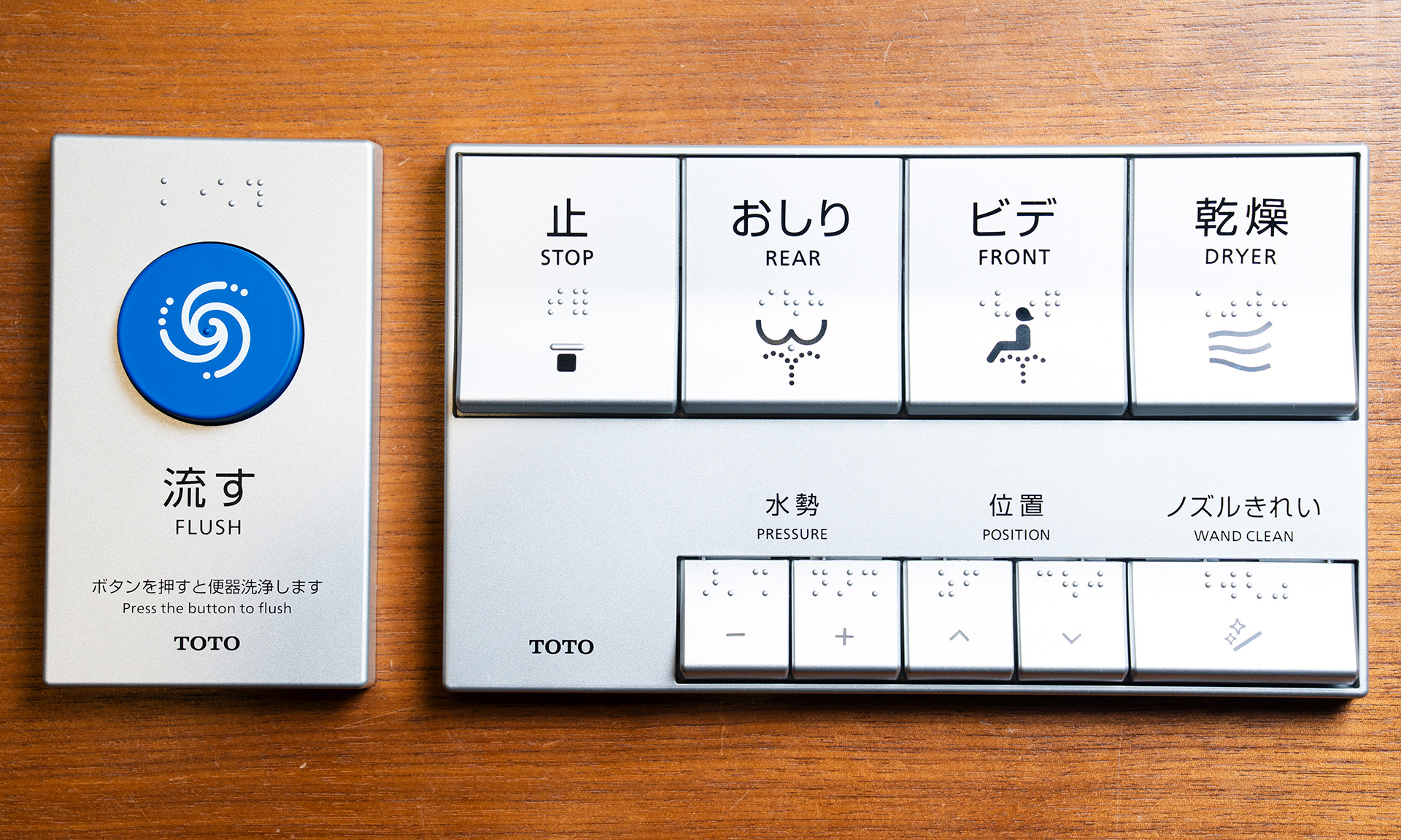 改良後のエコリモコン。便器洗浄リモコンとウォシュレットリモコンに分かれている。便器洗浄ボタンは大きな青い丸ボタンひとつだけで、下に大きな文字で「流す」と書かれている。改良前と比べてウォシュレットリモコンの上段のボタンの文字が大きくなり、下段の調節ボタンはボタン自体が小さくなっている
